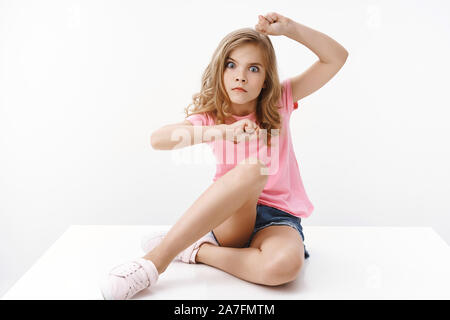 Playful funny pretty teenage blond girl, sit on floor, making serious grimace, stare camera shake raised hands, wanna scare with glance, fool around Stock Photo