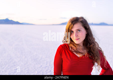 Bonneville Salt Flats near Salt Lake City, Utah at twilight sunset with purple pink salt and portrait of happy young woman girl in red shirt with hori Stock Photo