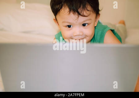 A male toddler is playing with a laptop while on the bed Stock Photo