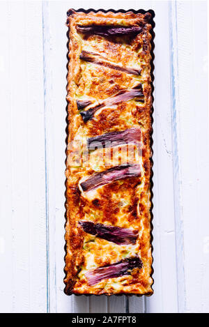 Salted cake with spring onion stripes, with fontina ,eggs, cream, and sausages, violet stripses atop, rectangular shapes on a dark background Stock Photo