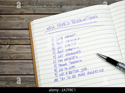 New Year's resolutions listed in a notpad. Wooden background. Stock Photo