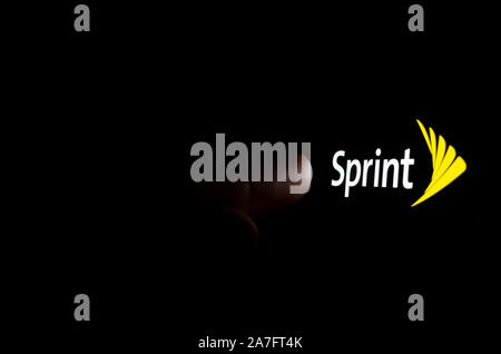 Sprint logo on a smartphone screen in a dark room and a finger touching it. Stock Photo