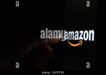 Amazon logo on a smartphone screen in a dark room and a finger pointing at it. Stock Photo