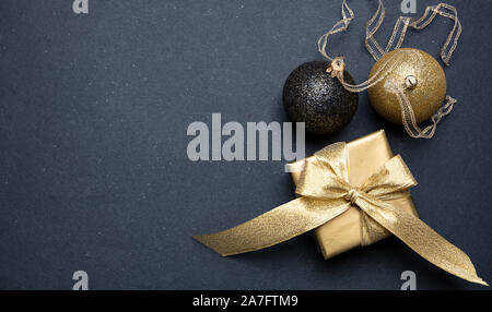 Gold and black Christmas decoration. Xmas balls and gift box shiny against dark gray background, high angle, copy space Stock Photo