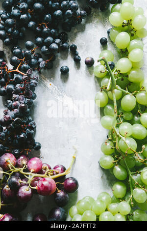 Three colors grapes biologically cultivated, sparsely arranged on a gray background, top view and flat lay composition Stock Photo