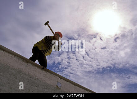 Industry. Construction.  Silhouette of man using sledgehammer on top of industrial building. Stock Photo