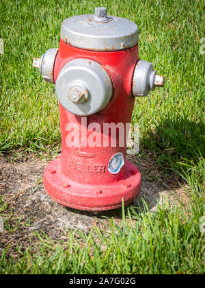 A bright red fire hydrant is installed on a grassy patch, ready for emergency use. Stock Photo