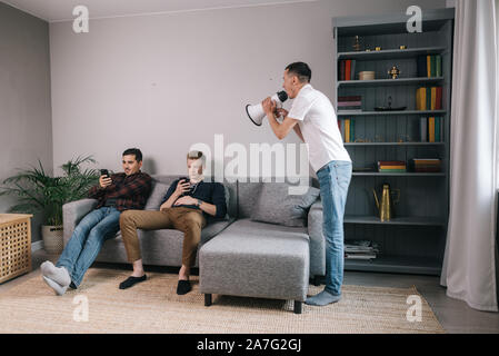 Young man yelling through megaphone at friends which using a mobile phone. Stock Photo