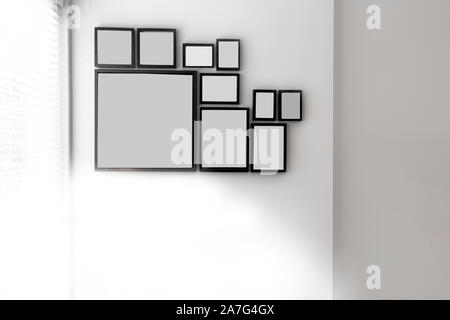 Group of various blank black picture frames on grey wall near a window with light, space for text Stock Photo