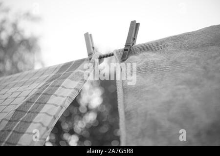 Two kitchen towels are dried on a clothesline with clothespins in the garden against the sky, bw photo. Stock Photo