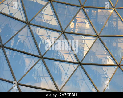 Abstract pattern of the roof of a geodesic dome, where each triangular panel has a reflection of the figures standing at railings inside the structure Stock Photo