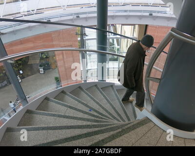 Man in woolly hat and brown winter jacket walking down the steps of the spiral staircase at the Victoria Gate shopping centre in Belfast city centre. Stock Photo