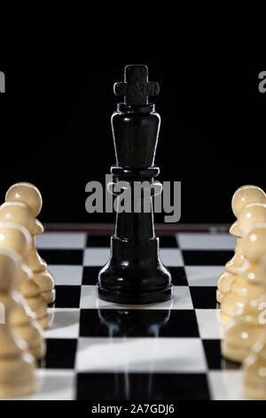 Black chess queen and army of white pawns on a chessboard on a black background Stock Photo