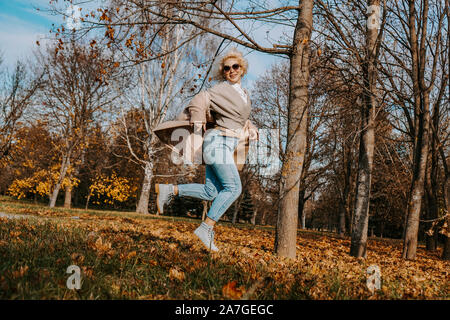 Beautiful woman in autumn park jumping and smiling - sunny day Stock Photo