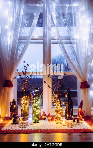Cute and warm Christmas decoration set with vintage beer bottles and wine bottles filled with micro led party lights, behind the window is countryside Stock Photo