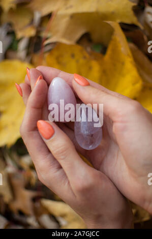 Female hands with orange manicure holding two yoni eggs made from pink quartz and transparent violet amethyst for vumfit, imbuilding or meditation on Stock Photo