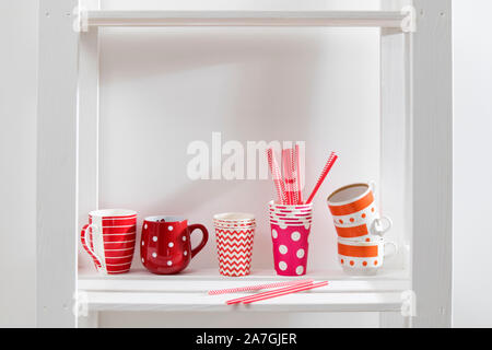 Different red mugs and glasses stand on a shelf in the kitchen Stock Photo