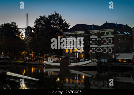 Calm scene of the old harbor of Gouda, Netherlands at dusk with dutch windmill in the background Stock Photo