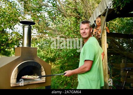 Man cooking artisanal pizza outdoors in a wood fired Forno Bravo oven, made with organic ingredients at Inn Serendipity, Browntown, Wisconsin, USA Stock Photo