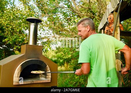 Man cooking artisanal pizza outdoors in a wood fired Forno Bravo oven, made with organic ingredients at Inn Serendipity, Browntown, Wisconsin, USA Stock Photo