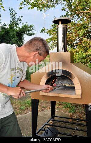 Man cooking artisanal pizza outdoors in a wood fired Forno Bravo oven, made with organic ingredients at Inn Serendipity, Browntown, Wisconsin, USA Stock Photo