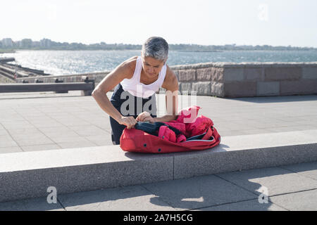 Middle-aged woman packing up yoga gear by ocean Stock Photo