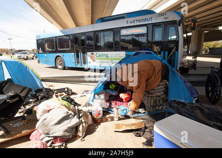 Days before a threatened crackdown by Texas Governor Greg Abbott on public right-of-way camping, homeless Texans including 'Corky',  await  the governor's and highway department actions. Most are unsure where they will go as local shelters are over capacity. An Austin city bus passes on the road just steps from the encampment. Stock Photo
