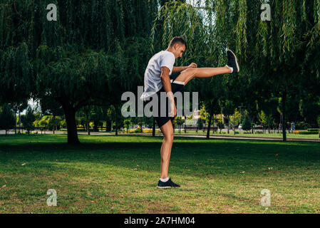 Runner in black sportswear stretching legs before doing morning workout Stock Photo