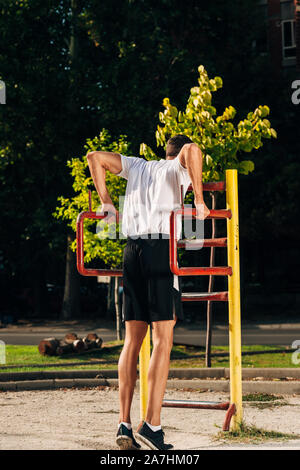 Crossfit man doing dips on chin-up bar during workout outdoors Stock Photo