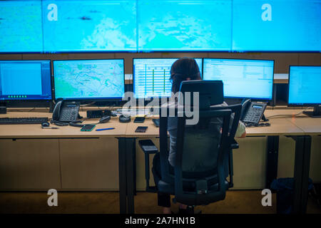 Female security guard sitting back and monitoring modern CCTV cameras in a surveillance room. Stock Photo