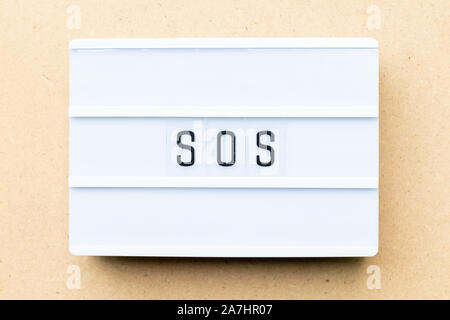 White lightbox with word SOS (abbreviation of save our soul/ship or sibling over shoulder) on wood background Stock Photo
