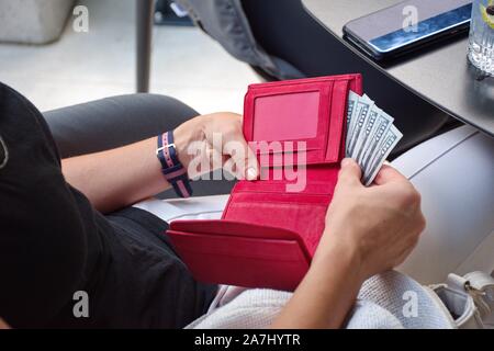 Midsection of the young woman paying bill in the restaurant. Red wallet with dollars Stock Photo