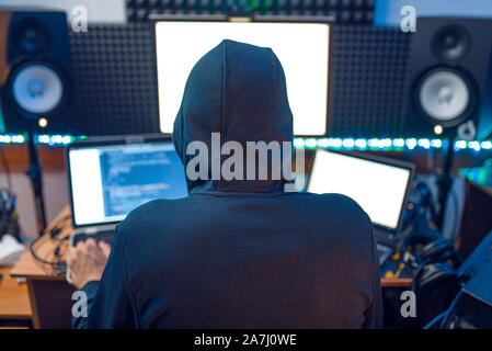 Hacker in the hood sitting at laptop, back view Stock Photo