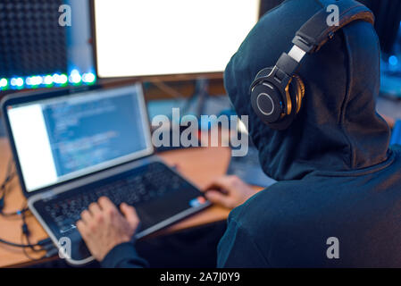 Hacker in the hood sitting at laptop, back view Stock Photo
