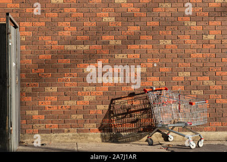 Abandoned shopping cart left behind against red brick wall. Stock Photo
