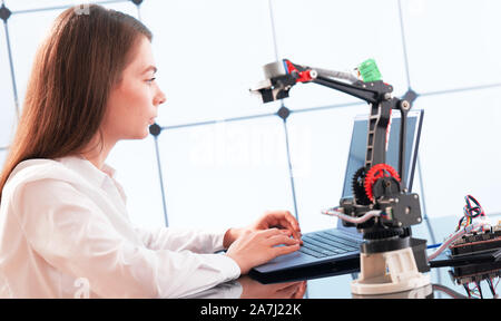 A young woman writes an algorithm for the robot arm. Science Research Laboratory for Robotic Arm Model. Computer Laboratory Stock Photo