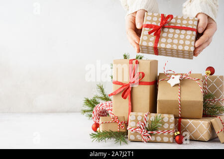 Young woman hands taking a beautifully decorated gift box from a big stack of gifts. Light gray background with space for text. Stock Photo