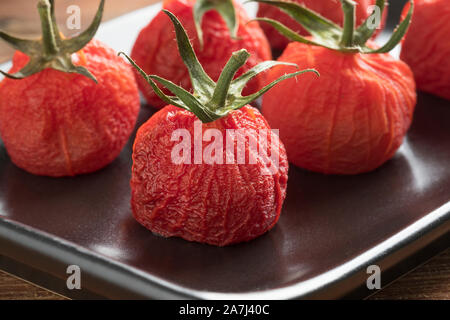 Roasted peeled red vine tomatoes with stem on a dish close up Stock Photo