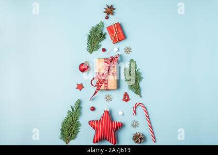 christmas tree made from fir branches, red decorations, candy, winter berries and gift boxes on blue background. holiday creative concept. new year or Stock Photo