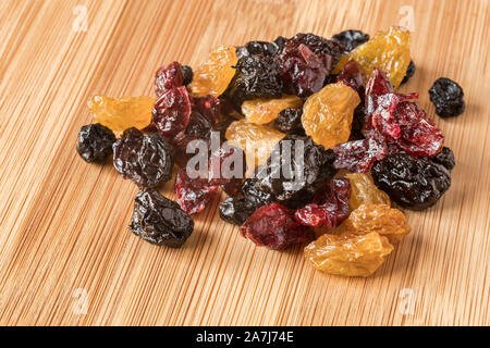 A handful of mixed dried fruit, with golden raisins, cherries, blueberries and cranberries, on a bamboo board. Stock Photo