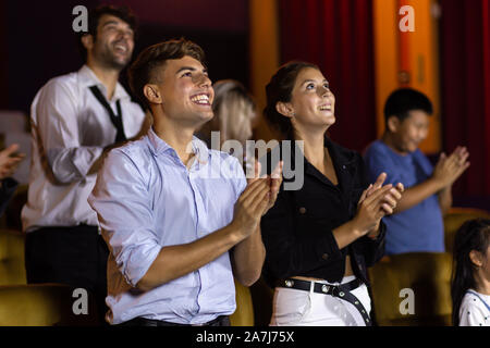 Amazed cheerful man and woman smiling and applauding while standing at seats in cinema hall after movie looking on stage Stock Photo