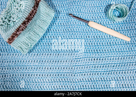 little beanie, crochet hook and yarn on blue crocheted cloth, handiwork workshop Stock Photo