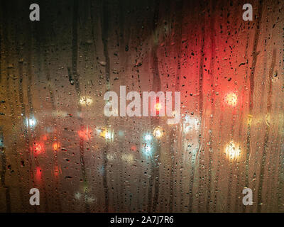 Raindrops on a bus window with blurred headlights behind Stock Photo