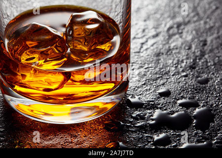 Glass of elegant whiskey with ice cubes on black stone table. Moody close up view Stock Photo