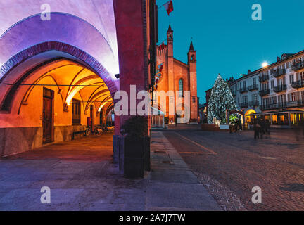 View of illuminated buildings and Christmas tree on cobblestone town square in evening in small town of Alba, Piedmont, Northern Italy. Stock Photo