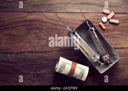 Vintage syringes, medical pills and rolled dollar bills on wooden table. Concept of drug addiction and trafficking. Stock Photo