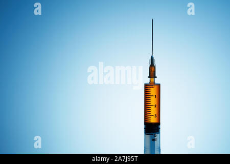 Syringe filled with orange liquid on blue background Stock Photo