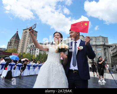 A couple take pictures of themselves by the Huangpu river in Shanghai, China, 19 September 2019.   15 couples held group weddings by the Huangpu river Stock Photo
