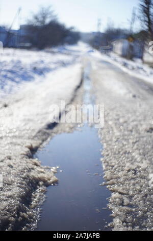 Difficult weather conditions. Winter sleet. Rural road in the snow with a puddle. Stock Photo