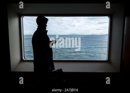 A young professional businessman on a ferry staying in touch texting on his cell phone. Stock Photo